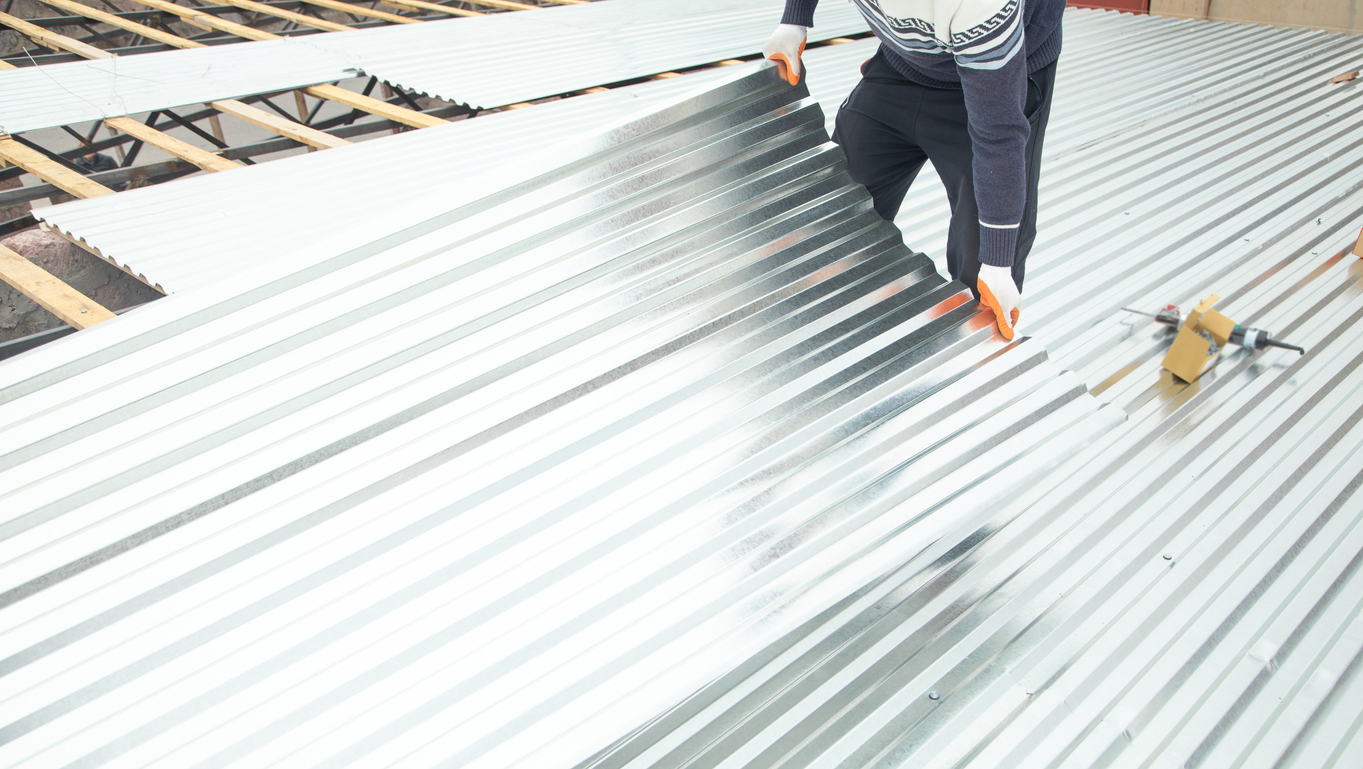 Worker puts the metal tiles on the roof of a house.